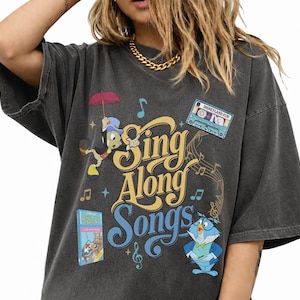May include: Dark gray t-shirt with a graphic design featuring the words "Sing Along Songs" in yellow and blue. The design includes cartoon characters, musical notes, and a cassette tape with the text "Disneyland Fun".