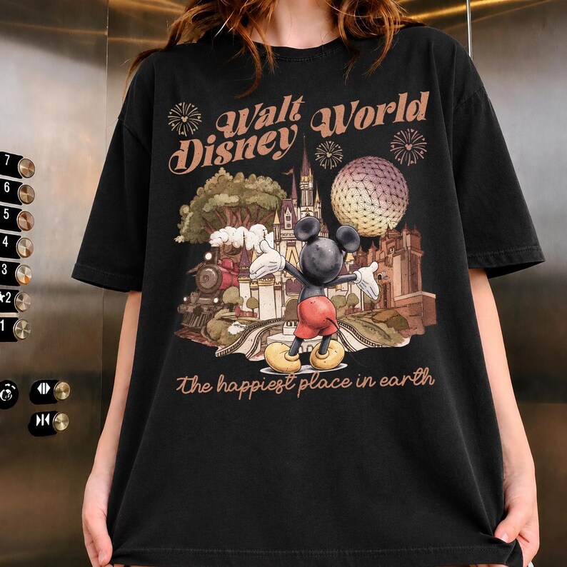 May include: Black t-shirt featuring a colorful graphic of Mickey Mouse in front of a Disney World scene. The text "Walt Disney World" and "the happiest place in earth" are also displayed on the shirt.