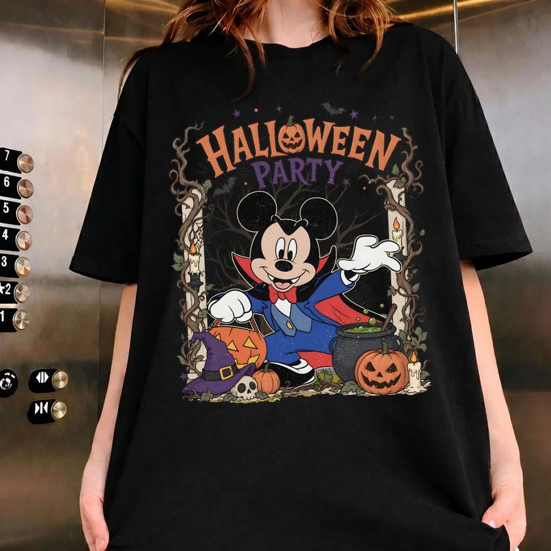 May include: A black t-shirt featuring a graphic of Mickey Mouse dressed as a vampire. The design includes the text "HALLOWEEN PARTY," pumpkins, a witch's hat, a skull, a cauldron, and lit candles framed by dark, twisted tree branches.
