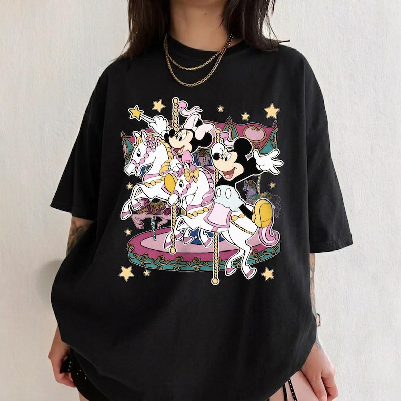 Puede incluir: Camiseta negra con un dise&ntilde;o de carrusel que presenta a los personajes de Mickey y Minnie Mouse montados en caballos blancos. El gr&aacute;fico incluye detalles en rosa, amarillo y azul, con motivos de estrellas. Una camiseta gr&aacute;fica divertida y caprichosa.