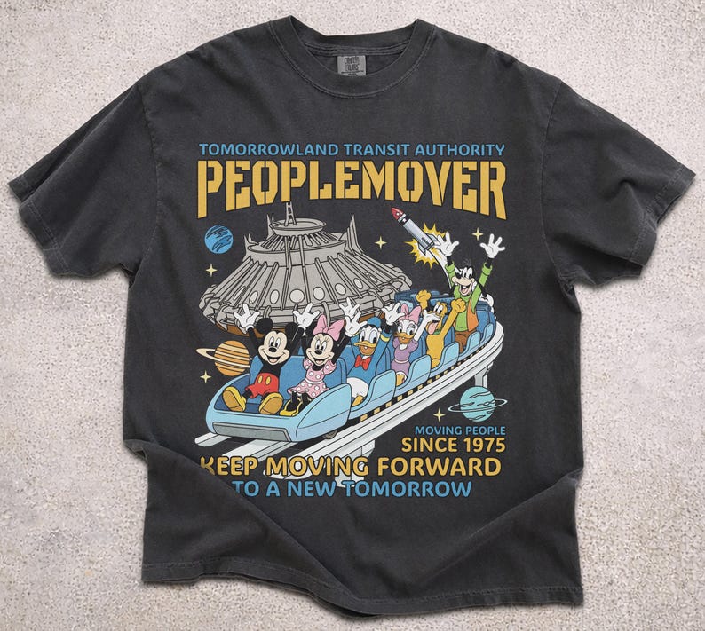 May include: Dark gray t-shirt featuring a colorful graphic of the PeopleMover ride with Mickey Mouse, Minnie Mouse, Donald Duck, Daisy Duck, and Goofy. The text reads "Tomorrowland Transit Authority PeopleMover" and "Keep Moving Forward to a New Tomorrow."