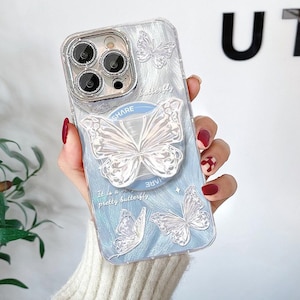 May include: Clear phone case with a light blue background and white butterfly designs. The case has a pop-up butterfly grip that says "SHARE". The text "It is a very pretty butterfly" is also visible.