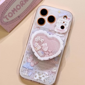 May include: A clear phone case featuring a heart-shaped shaker attachment filled with small charms. The case is decorated with pastel stickers of a puppy, a butterfly, stars, and bows. A pink box with the word TOMORROW is positioned nearby.