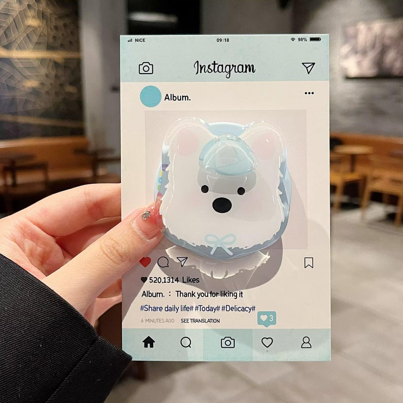 May include: A light blue Instagram-themed card featuring a cartoon bear-shaped phone grip. The grip is white with a blue hat and bow. The card includes the Instagram logo, the word "Album", and the text "Thank you for liking it".