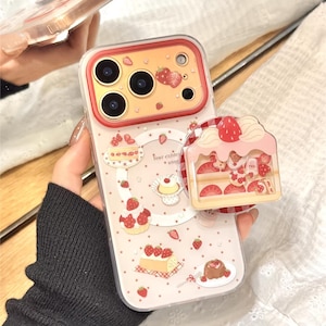May include: A clear phone case with a strawberry and dessert theme. The case features illustrations of cakes, strawberries, and the text "Your existing utopia". A matching strawberry cake phone grip is attached.