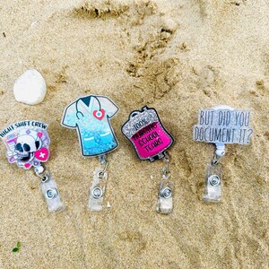 K&ouml;nnte beinhalten: Vier Ausweishalter aus Acryl mit einziehbaren Clips. Einer zeigt einen Totenkopf mit dem Text Night Shift Crew, einer ist ein blaues Glitzer-Kasack-Oberteil, einer ein pinker Glitzer-Infusionsbeutel mit 100% Nursing School Tears und einer But Did You Document It?