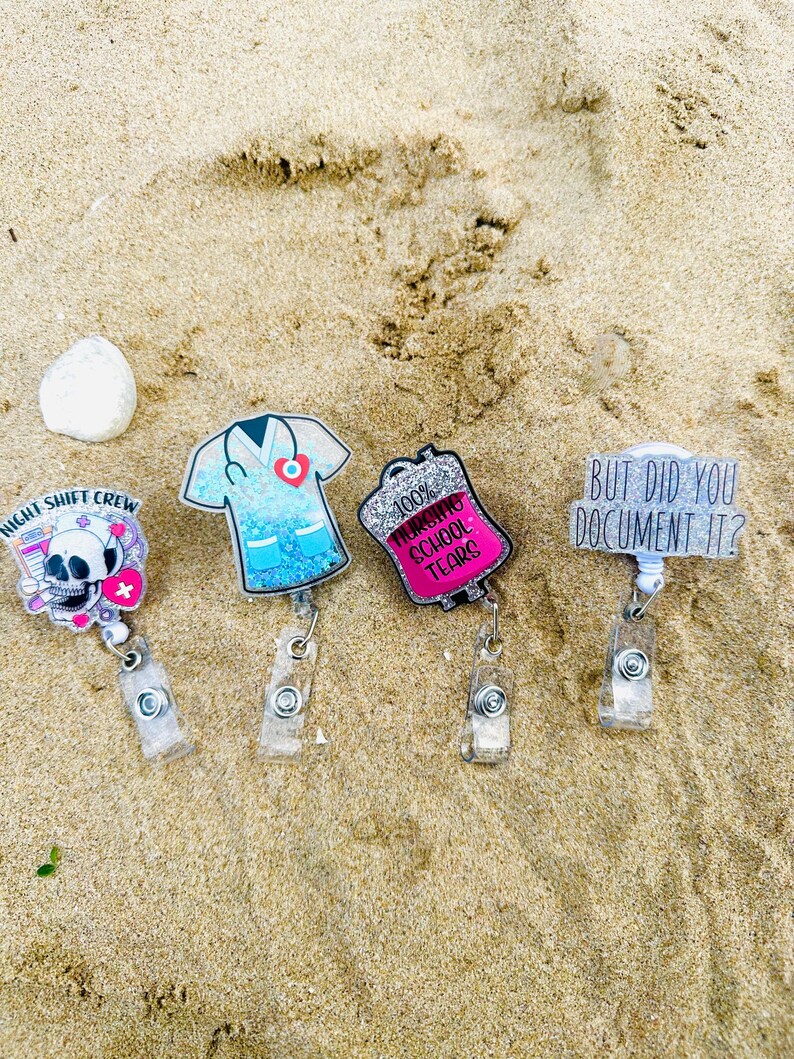 K&ouml;nnte beinhalten: Vier Ausweishalter aus Acryl mit einziehbaren Clips. Einer zeigt einen Totenkopf mit dem Text Night Shift Crew, einer ist ein blaues Glitzer-Kasack-Oberteil, einer ein pinker Glitzer-Infusionsbeutel mit 100% Nursing School Tears und einer But Did You Document It?