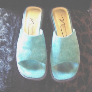 May include: A pair of light blue open-toe slide sandals with a textured finish. The interior footbed is light-colored and features the brand name Newport News printed in black script. The soles are dark-colored with a rounded toe shape.