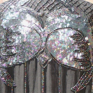 May include: Black evening top with iridescent sequin and bead embellishments. The top features a detailed design on the bodice and sleeves, with a square neckline and a flowing, sheer fabric. The sequins shimmer with multiple colors.