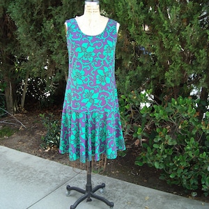 Puede incluir: Un vestido sin mangas con estampado floral morado y verde. El vestido tiene un corpiño ajustado y una falda acampanada.