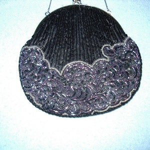 May include: A black beaded evening bag with a silver chain handle. The bag has a rounded shape with a scalloped edge. The bottom edge features a decorative, swirling pattern in shades of purple and silver.