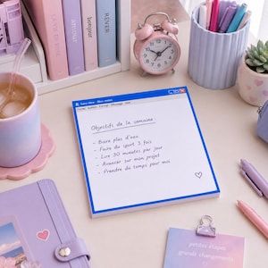 Peut inclure: Une scène de bureau avec un réveil rose, des stylos et une plante succulente dans un pot à motifs de cœur. Un bloc-notes avec le texte "Objectifs de la semaine" et une boisson dans une tasse pastel sont également présents.