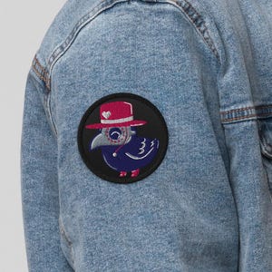 May include: A light blue denim jacket with a white sherpa collar and a black patch featuring a cartoon crow wearing a red hat and sunglasses.