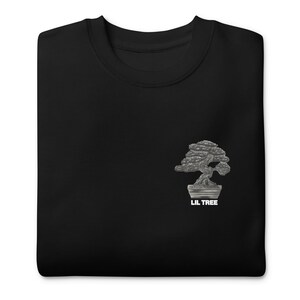 Może przedstawiać: Czarna bluza z okrągłym dekoltem z srebrnym wzorem drzewka bonsai. Pod drzewkiem wydrukowano napis "LIL TREE". Bluza wykonana jest z miękkiego materiału.