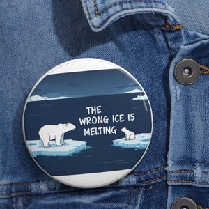 May include: A round button with a polar bear and cub on ice floes, set against a dark blue sea and sky. The text "THE WRONG ICE IS MELTING" is displayed in white. The button is set against a denim background.