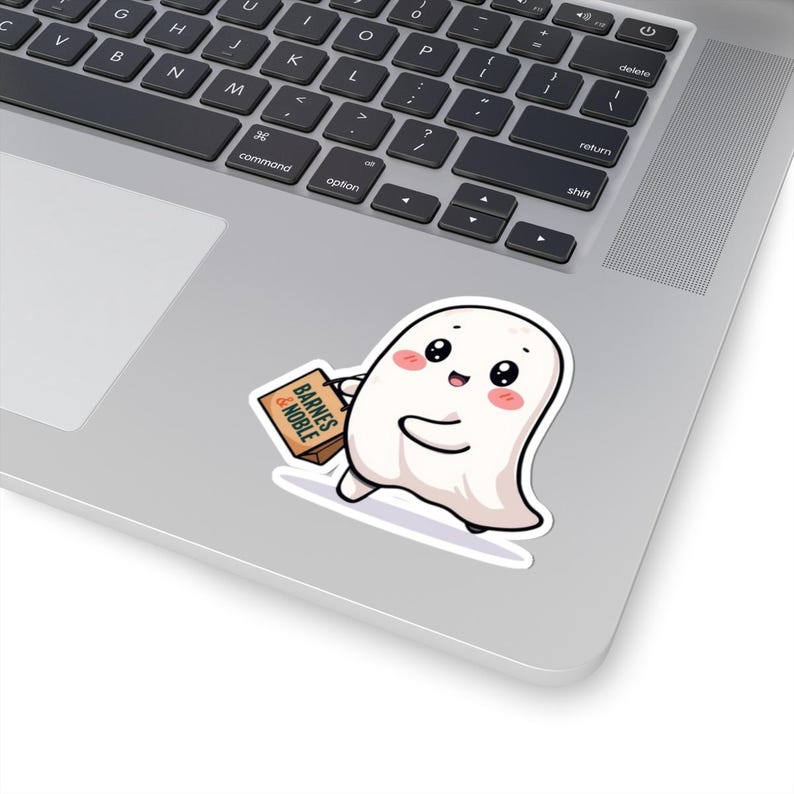 K&ouml;nnte beinhalten: Ein wei&szlig;er Geisteraufkleber mit einem l&auml;chelnden Gesicht und rosigen Wangen, der eine braune Schachtel mit der Aufschrift "BARNES & NOBLE" tr&auml;gt. Der Aufkleber befindet sich auf einem Laptop und deutet auf ein Produkt oder Design zum Thema B&uuml;cher hin.