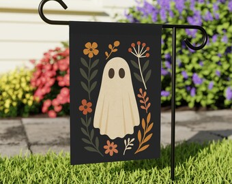 May include: Black garden flag featuring a beige ghost with oval eyes, surrounded by orange and beige flowers and leaves. The flag is displayed on a black metal stand, perfect for Halloween or fall decor.