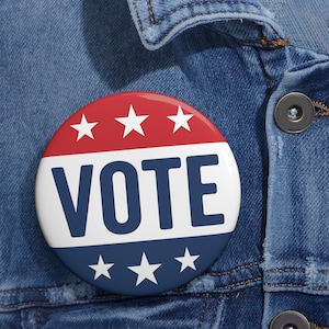 May include: A round button with a red, white, and blue design. The top section is red with three white stars, the middle is white with the word "VOTE" in navy blue, and the bottom is blue with three white stars. The button is pinned to a denim jacket.