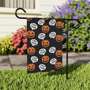 Può includere: Bandiera da giardino nera di Halloween con un motivo ripetuto di zucche arancioni e fumetti bianchi con il testo "FUCK TRUMP". La bandiera è esposta su un supporto di metallo nero in un giardino.