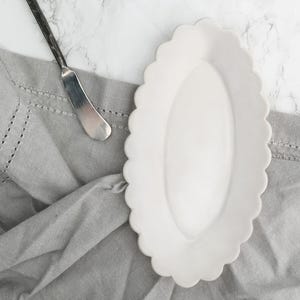 May include: A white ceramic butter dish with a scalloped edge. The dish is oval shaped and has a smooth, glossy finish.