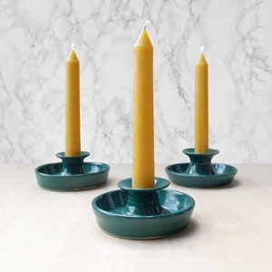 May include: Three teal ceramic candle holders with a single yellow beeswax candle in each.