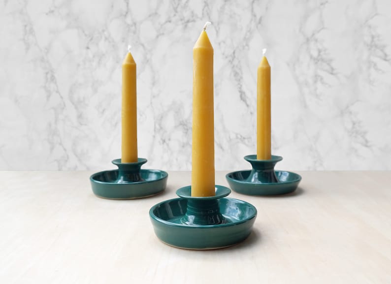 May include: Three teal ceramic candle holders with a single yellow beeswax candle in each.