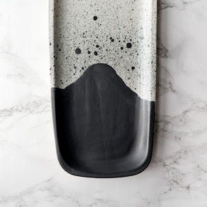 May include: A black and white ceramic serving tray with a speckled white glaze and a black glaze on the bottom half. The tray is rectangular with rounded edges.