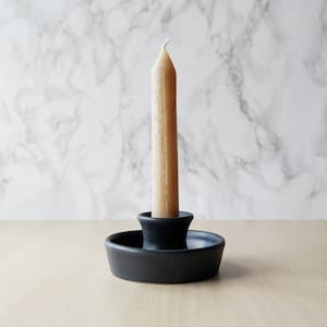 May include: A black ceramic candle holder with a single, off-white candle.