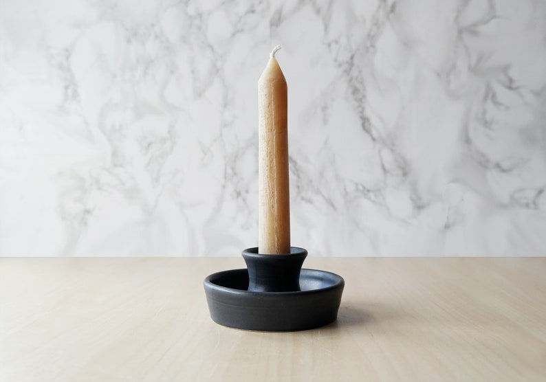 May include: A black ceramic candle holder with a single, off-white candle.