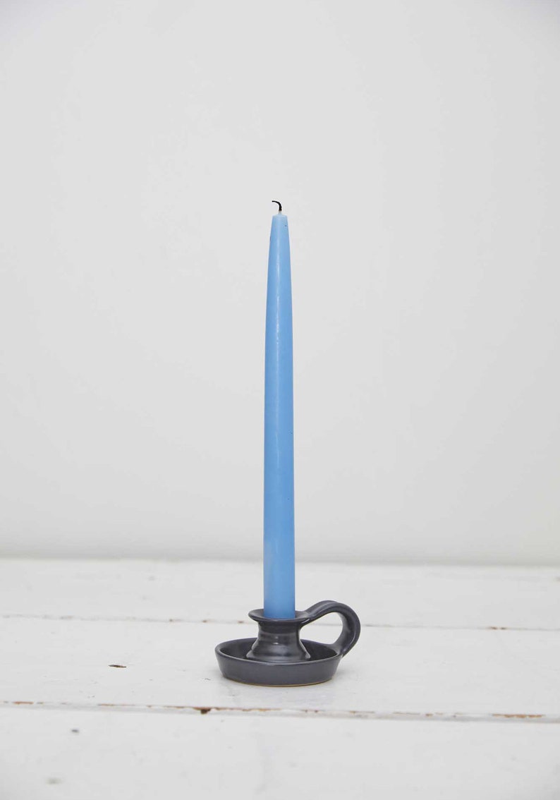 May include: A blue candle in a gray ceramic candlestick with a handle.