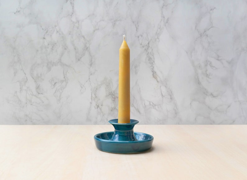 May include: A teal ceramic candle holder with a single yellow candle.