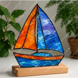 Puede incluir: Una escultura de velero de vidrieras con velas naranjas y azules, colocada sobre una base de madera. El vidrio tiene una apariencia texturizada, con la palabra "vitraluz" repetida en la imagen. Un artículo náutico decorativo.