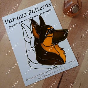 Puede incluir: Una hoja de papel con el texto "Vitraluz Patterns" y un diseño de perro en marrón y naranja. Una pequeña botella de vidrio naranja con un tapón de corcho está en el fondo. El diseño es solo para uso personal.