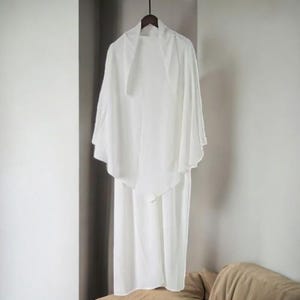 May include: A white, long-sleeved, lightweight, open-front cardigan with a draped design. The cardigan is hanging on a hanger.