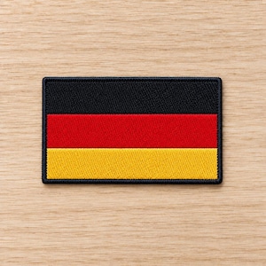 May include: A rectangular embroidered patch featuring the flag of Germany. The design consists of three horizontal stripes in black, red, and gold, with a thick black stitched border surrounding the entire perimeter of the fabric emblem.
