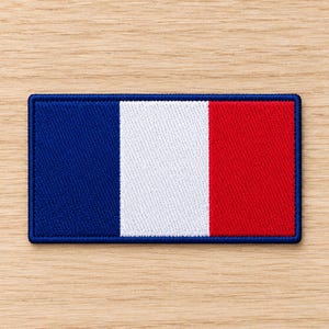 Peut inclure: Un écusson rectangulaire brodé représentant le drapeau national français avec trois bandes verticales bleu, blanc et rouge. L'écusson présente une bordure cousue bleu foncé qui encadre le motif tricolore, créant un bord net et défini.