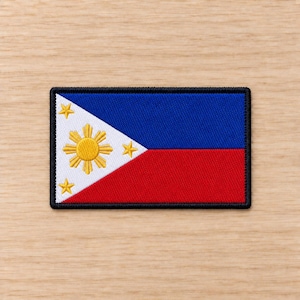 Könnte beinhalten: Ein rechteckiger, bestickter Aufnäher mit der Flagge der Philippinen. Das Design zeigt ein weißes Dreieck auf der linken Seite mit einer gelben Sonne und drei gelben Sternen sowie horizontale blaue und rote Streifen, alles schwarz umrandet.