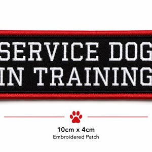 Puede incluir: Un parche rectangular bordado con fondo negro y borde rojo. El texto SERVICE DOG IN TRAINING está cosido en letras mayúsculas blancas. Debajo del parche, el texto indica unas dimensiones de 10cm x 4cm y una huella de pata roja.