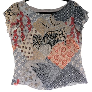 Könnte beinhalten: Eine Bluse im Patchwork-Stil mit rundem Ausschnitt und kurzen, gerüschten Ärmeln. Das Oberteil hat eine Vielzahl von gemusterten Stoffquadraten in Beige-, Rot-, Grau- und Schwarztönen. Das Design umfasst Blumen-, Paisley- und geometrische Motive.