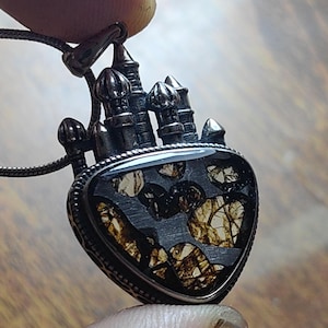 Puede incluir: Un collar con un colgante de plata en forma de castillo y una piedra triangular marrón y blanca. La piedra tiene un patrón único y moteado.