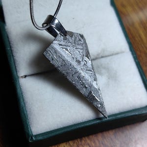 Peut inclure: Un collier avec un pendentif en forme de triangle en météorite argenté. Le pendentif présente un motif unique de lignes et de tourbillons.