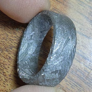 May include: A silver ring with a textured surface. The ring is made of metal and has a smooth, rounded edge.