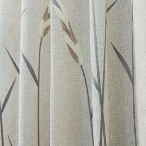 May include: Close-up of a beige curtain with a botanical design. The curtain features a repeating pattern of stylized cattails in shades of brown, white, and grey. The fabric has a textured appearance, and the design is printed on the surface.