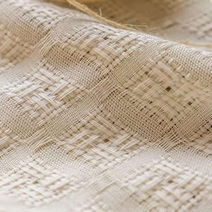 Puede incluir: Primer plano de una tela tejida con un patrón texturizado de tejido de cesta. La tela es de color beige neutro, con hilos visibles que crean un diseño similar a una cuadrícula. Un trozo de cuerda es visible en la parte superior de la imagen.