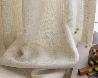 May include: Off-white linen curtains with a textured weave, draped in soft folds. The fabric has a subtle, natural appearance. The image also shows a book and wooden blocks.