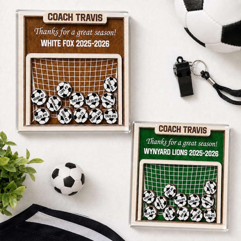 May include: Two square wooden display frames featuring a soccer goal graphic with small soccer ball tokens labeled with names and numbers. Each frame is engraved with COACH TRAVIS, Thanks for a great season!, and team names WHITE FOX or WYNYARD LIONS 2025-2026.