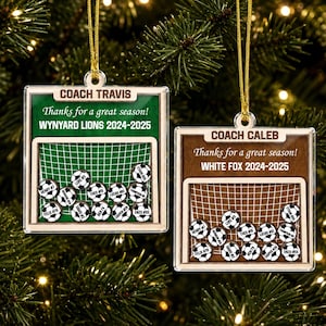May include: Two square wooden ornaments featuring a soccer goal graphic. One has a green background with text COACH TRAVIS, Thanks for a great season! WNYARD LIONS 2024-2025. The other has a brown background with COACH CALEB, Thanks for a great season! WHITE FOX 2024-2025. Both include small soccer ball tokens with names and numbers.
