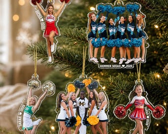 May include: Five clear acrylic ornaments featuring cheerleaders. One shows a single cheerleader with text 'SOPHIA 2026'. Another shows a squad with 'SHIMMER SQUAD 2026'. A third shows a cheerleader with 'SARAH 2026'. Others show groups and a cheerleader with 'SARAR 2026'.
