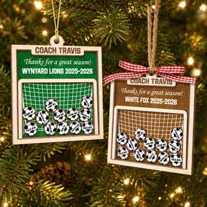 May include: Two square wooden ornaments featuring a soccer goal graphic. The left ornament is green with text reading COACH TRAVIS, Thanks for a great season!, WYNYARD LIONS 2025-2026. The right is brown with a red gingham bow and matching text.