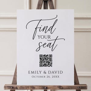 May include: A white sign on a wooden easel, featuring the words "Find Your Seat" in black script. A QR code is below the text, with the names "Emily & David" and the date "October 26, 20XX".